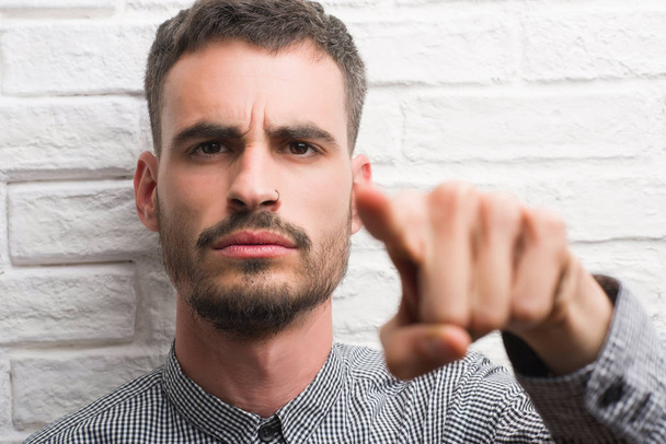 Молодой взрослый мужчина, стоящий над белой кирпичной стеной, указывая пальцем на камеру и на вас, знак руки, позитивный и уверенный жест спереди
 - Фото, изображение