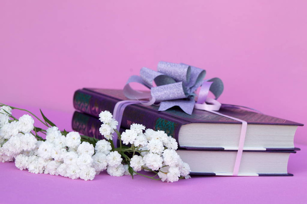 Bücher als Geschenk auf rosa Hintergrund dekoriert mit einer Schleife und einem Strauß Blumen weiße Zigeunerin - Foto, Bild