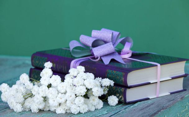 Bücher als Geschenk auf grünem Hintergrund mit Schleife und einem Strauß weißer Blumen - Foto, Bild