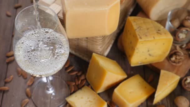 Ruokataidetta. Erilaisia juustoja kauniisti järjestetty puinen tausta. Huippunäkymä. Valkoviiniä kaadetaan lasiin. Erittäin hidas liike
. - Materiaali, video