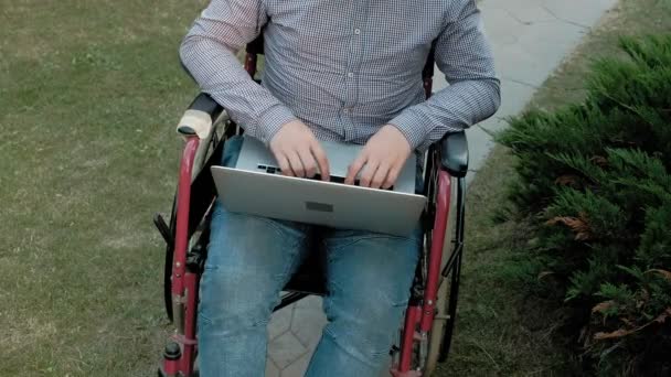 Ένας άνθρωπος με αναπηρία είναι κάθεται σε μια αναπηρική καρέκλα και να εργάζονται σε ένα φορητό υπολογιστή στο πάρκο - Πλάνα, βίντεο