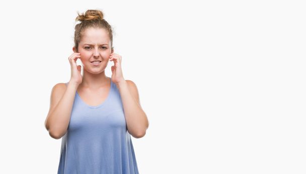 Young blonde woman covering ears with fingers with annoyed expression for the noise of loud music. Deaf concept. - Photo, Image