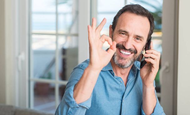 Mann mittleren Alters mit Smartphone tut ok Zeichen mit Fingern, ausgezeichnetes Symbol - Foto, Bild