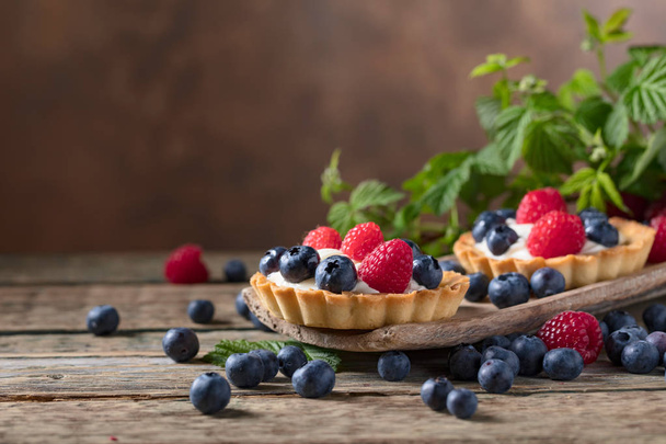  Dessert tarts with raspberries and blueberries on a wooden table. Closeup of fancy gourmet fresh berry dessert tarts. - Φωτογραφία, εικόνα