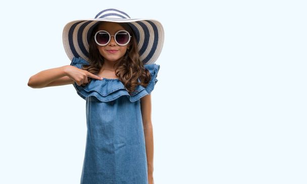 Güneş gözlüğü ve kendisi için sürpriz yüz işaret parmağı ile yaz şapka giymiş esmer Latin kız - Fotoğraf, Görsel