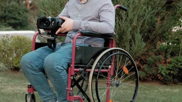 A disabled man in a wheelchair chair dresses a virtual reality helmet - Footage, Video
