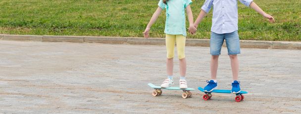 the girl holds the boy's hand, they together skateboard in the city park in the summer - Фото, зображення