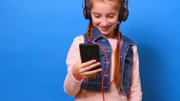 Little girl in headphones watching phone screen and smiling - Metraje, vídeo