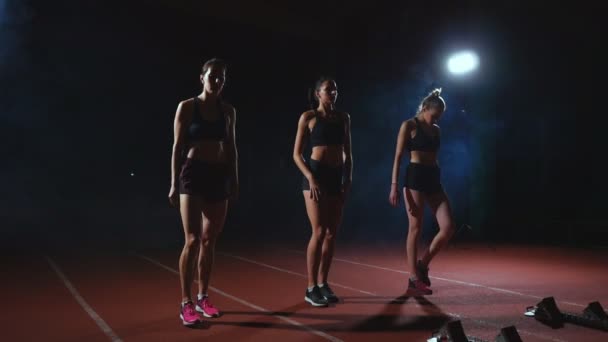 Tres chicas vestidas de negro están en las almohadillas de salida para comenzar la carrera en la competencia a la luz de las luces y correr hacia la meta
 - Imágenes, Vídeo