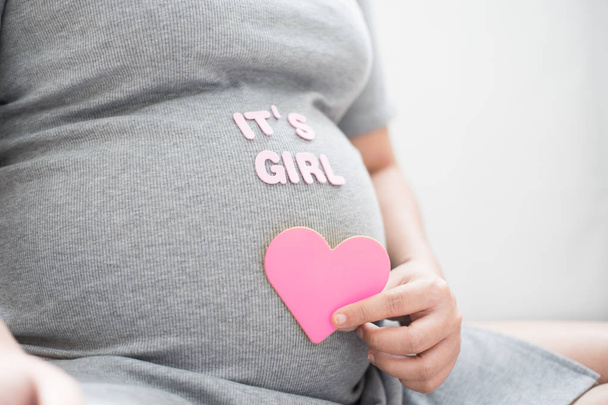 Mulher grávida com coração rosa e é tex menina na barriga. Conceito de chuveiro do bebê menina
. - Foto, Imagem
