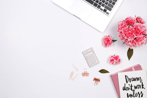 Γυναίκα χώρου εργασίας με laptop, σημειωματάριο χειρόγραφες απόσπασμα, ροζ λουλούδι γαρίφαλων σε άσπρο φόντο. Επίπεδη lay, κορυφαία θέα. Κομψά γυναικεία blogger έννοια. άνοιξη καλοκαίρι φόντο. - Φωτογραφία, εικόνα