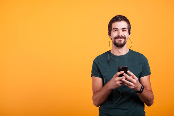 Szczęśliwy uśmiechający się człowiek z słuchawkami na słuchanie muzyki na swoim smartfonie - Zdjęcie, obraz