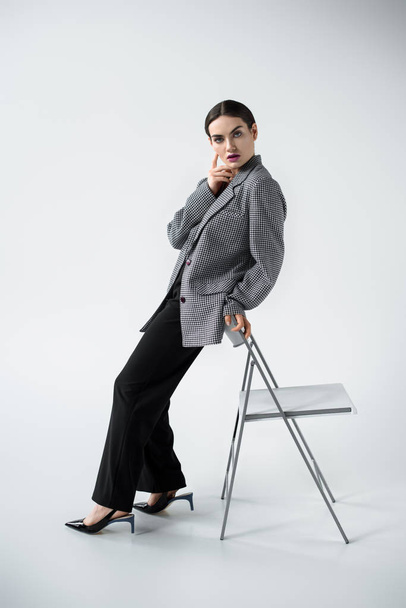 glamour fashionable woman posing in retro suit near chair, on grey  - Фото, зображення