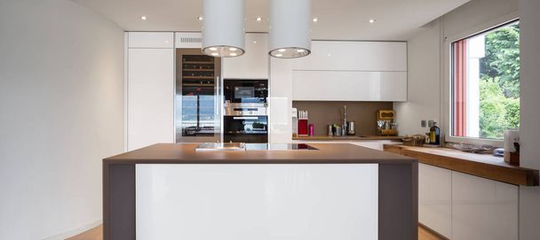 Kitchen with white island with hood and spotlights in modern apartment. Nobody inside - Foto, afbeelding