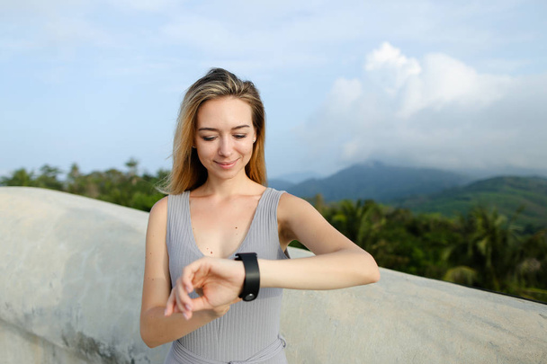junges amerikanisches Mädchen schaut auf intelligente Uhr, grüne Münder im Hintergrund. - Foto, Bild