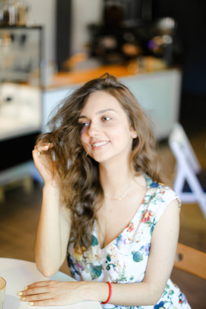 junge hübsche Frau sitzt im Café und berührt lockiges Haar. - Foto, Bild