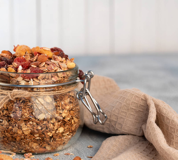 Healthy breakfast - glass jars of oat flakes, granola with dried fruit, berries and nuts on light background . - Photo, Image