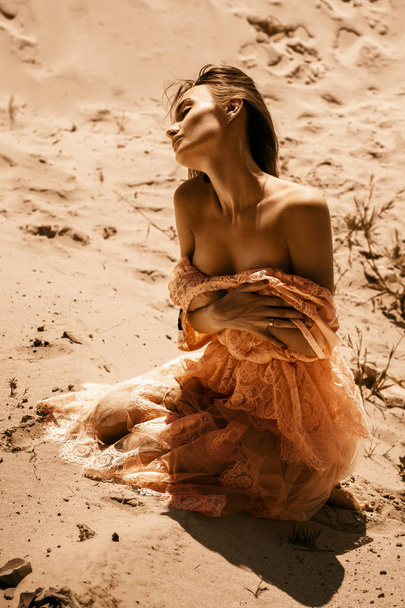 gorgeous lady wth closed eyes in pink dress sits in a hot desert - 写真・画像