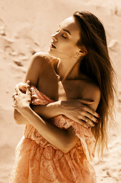 Sensual young woman with closed eyes in pink dress posing in a desert - Foto, Bild