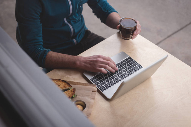 Середина людини, що використовує ноутбук у кафе
 - Фото, зображення