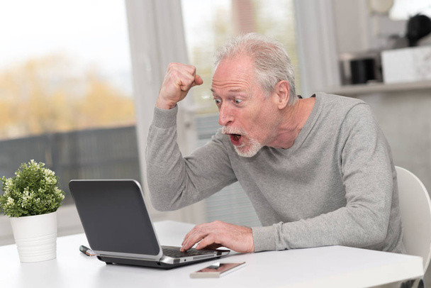 Happy mature man having an amazing surprise on laptop - Foto, afbeelding