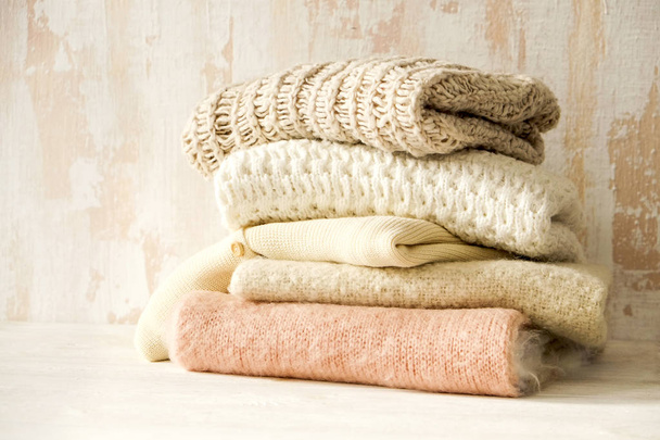 Bunch of knitted warm pastel color sweaters, different knitting patterns folded in messy stack on brown wooden table, grunged texture wall background. Fall winter season knitwear. Close up, copy space - Fotografie, Obrázek