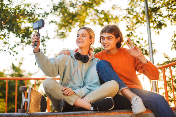 Joven patinador sonriente chico y chica con auriculares grabando felizmente un nuevo video juntos en skatepark
  - Foto, imagen