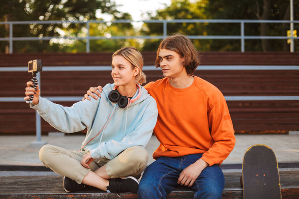 Νέοι σκέιτερ αγόρι και κορίτσι με ακουστικά εγγραφή νέου βίντεο χαρωπά να ξοδέψετε χρόνο μαζί στο skatepark  - Φωτογραφία, εικόνα