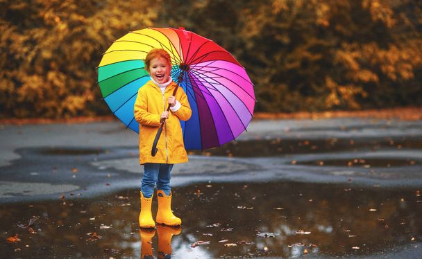 glückliches Kindermädchen mit Regenschirm und Gummistiefeln in einer Pfütze auf einem herbstlichen Wandbild - Foto, Bild