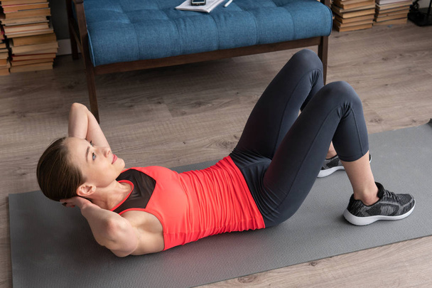 Mujer de fitness haciendo ejercicios abdominales en el suelo en casa
 - Foto, Imagen