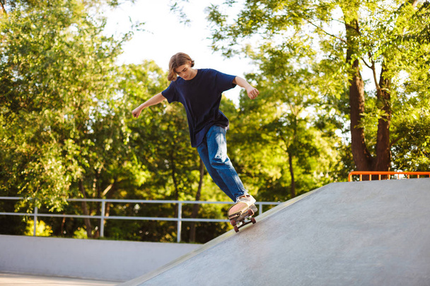 Jovem em T-shirt skate e praticando acrobacias passar tempo no skatepark moderno com bela vista sobre o fundo
 - Foto, Imagem