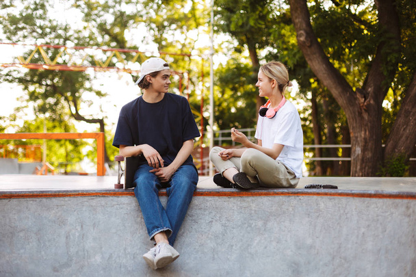 Pretty girl and young guy happily talking spending time together at modern skatepark  - Foto, afbeelding