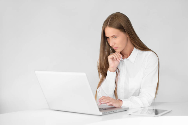 Giovane bella donna sta lavorando su un computer portatile in ufficio su uno sfondo bianco
. - Foto, immagini