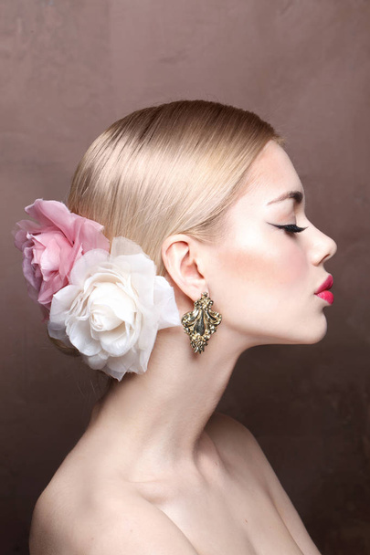 Fashion portrait of young blonde model with pink lips and roses in her hair wearing vintage earrings, side view - Foto, immagini