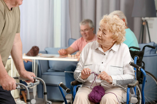 Femme âgée en tricot en fauteuil roulant tout en parlant avec son ami à la maison de soins
 - Photo, image