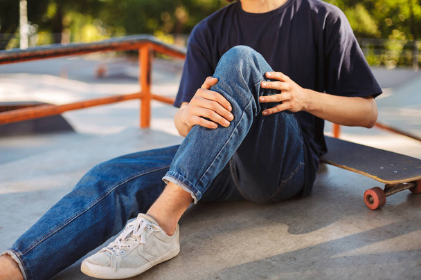 Skater trzymający nogę bolesne z deskorolka w pobliżu skatepark z bliska - Zdjęcie, obraz