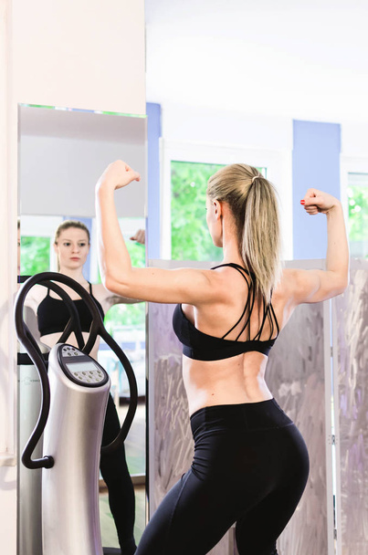 Joven hermosa mujer posando delante de un espejo en la placa de alimentación, buscando fuerte y saludable
. - Foto, imagen
