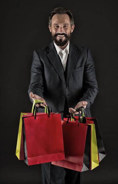 Happy to share. Man mature shopper carries shopping bags black background. Successful businessman choose only luxurious brands and shopping in high fashioned boutiques. Gifts for colleagues - 写真・画像