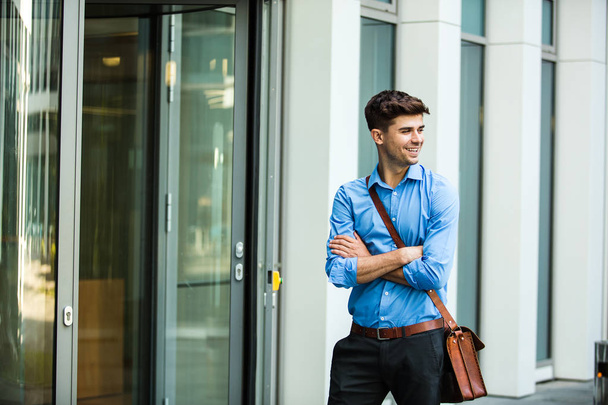 confident and successful antrepreneur, office man or corporate guy, standing with his leather bag and elegant outfit in front of an office building - Фото, изображение