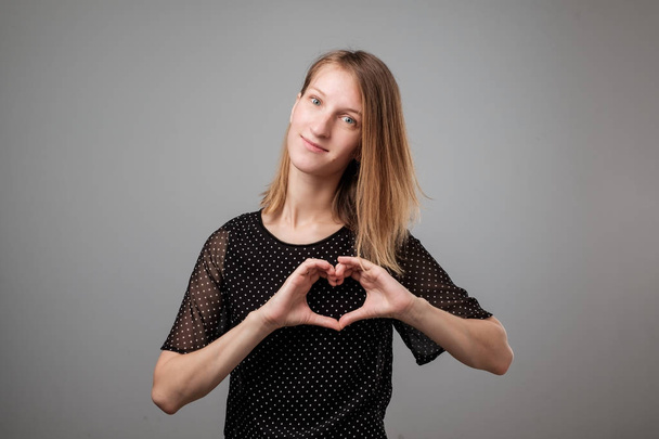 Portrait of a smiling young european woman showing heart gesture with two hands and looking at camera - Foto, afbeelding