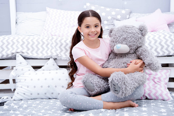 Favorite toy. Girl child sit on bed hug teddy bear in her bedroom. Kid prepare to go to bed. Pleasant time in cozy bedroom. Girl kid long hair cute pajamas relax and play plush teddy bear toy - Photo, Image
