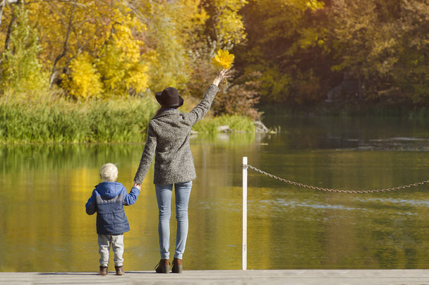 Mutter und Sohn stehen auf der Seebrücke am Fluss. Herbst, sonnig. zurück - Foto, Bild
