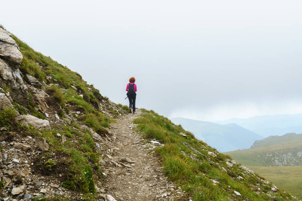 Caucasian woman hiker with backpack walking a trail in rocky mountains - Fotoğraf, Görsel