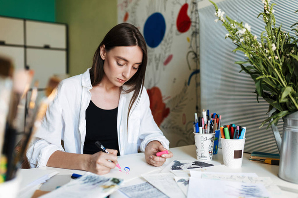 Mladý malíř zamyšleně u stolu, zasněně kreslení s růžový značka tráví čas v kreativní pracovišti doma  - Fotografie, Obrázek