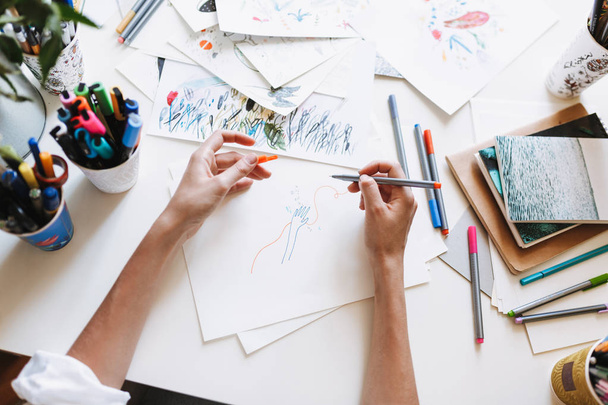 Εσωτερικη κορίτσι σχέδιο με χρωματιστά μαρκαδόρους σε χαρτί με εικόνες και σημειωματάρια στο γραφείο στο σπίτι  - Φωτογραφία, εικόνα