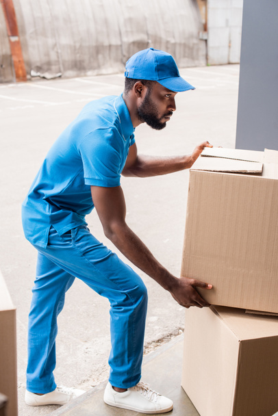 side view of african american delivery man putting boxes on pile - 写真・画像