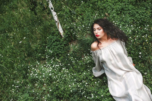 chica rizada en un vestido de sol se encuentra en la hierba con flores blancas
 - Foto, imagen