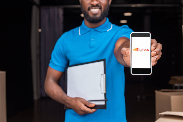 cropped image of african american delivery man showing smartphone with loaded aliexpress page - Foto, Imagen