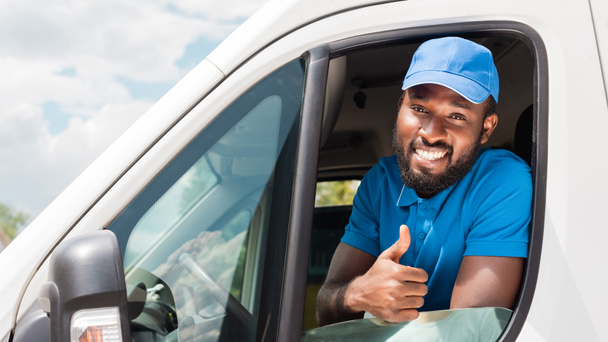 smiling african american delivery man showing thumb up from van - Fotó, kép
