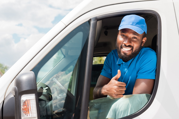 улыбающийся афроамериканец-курьер, показывающий большой палец из машины
 - Фото, изображение